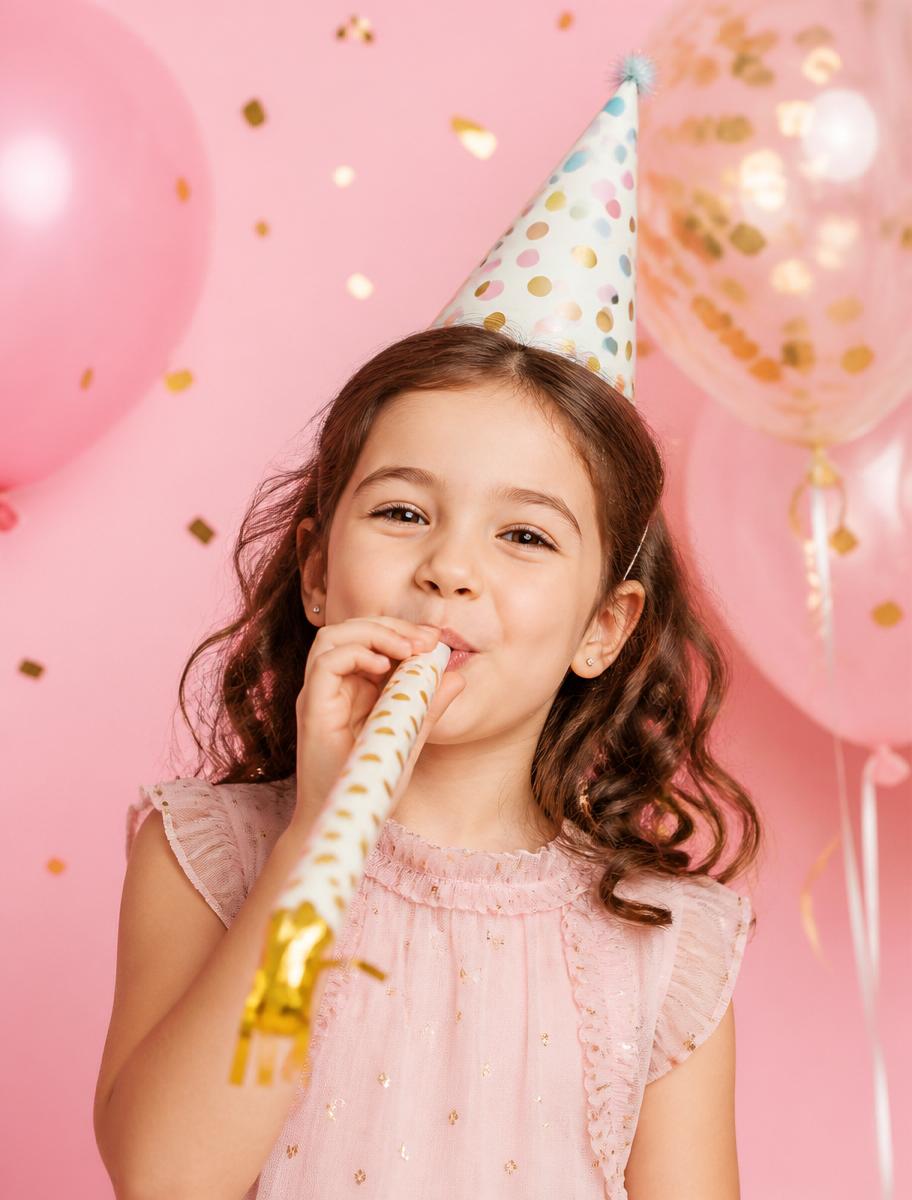 Bambina che soffia in una trombetta di compleanno